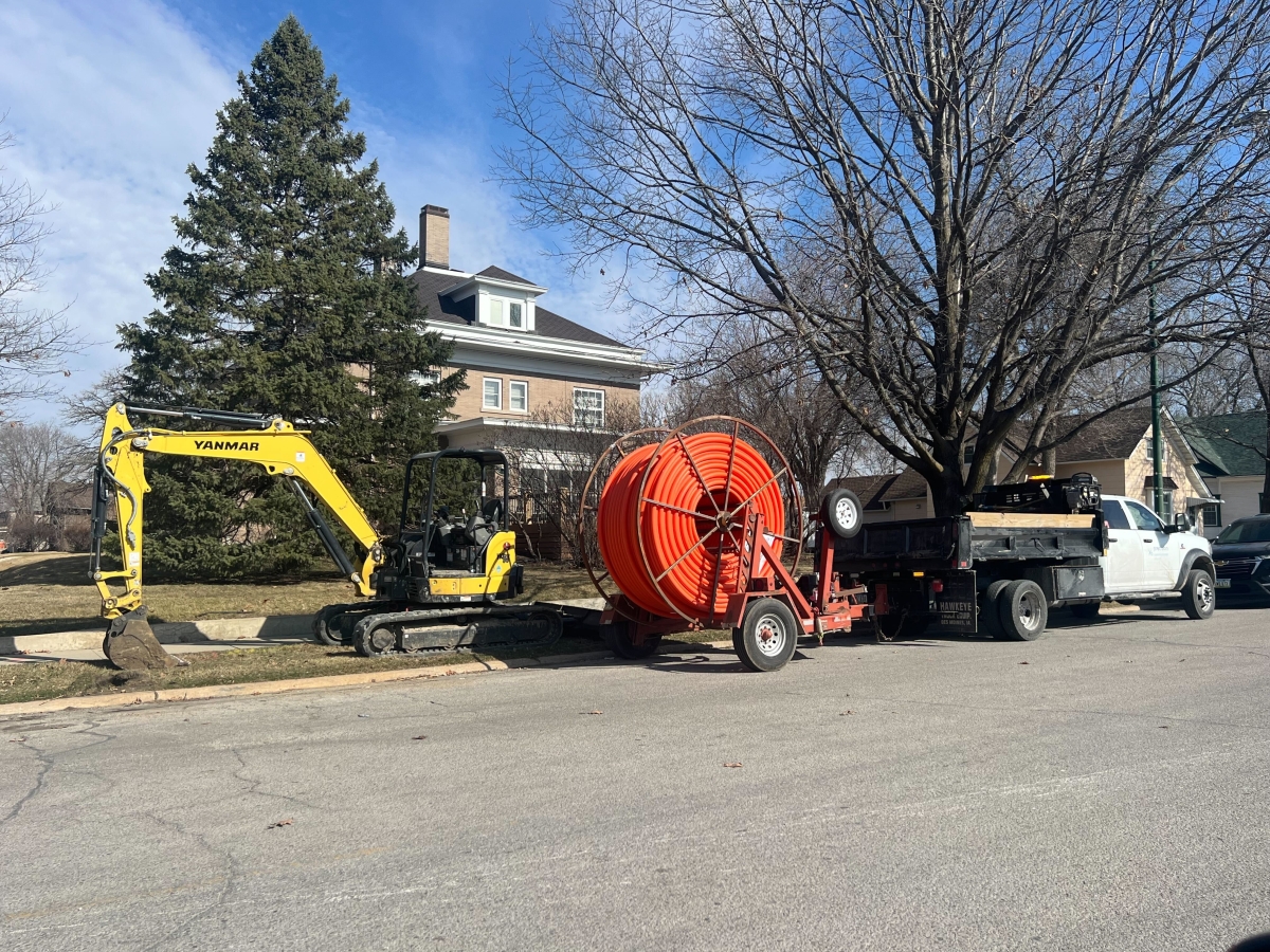 Backhoe with truck installing roll of fiber conduit